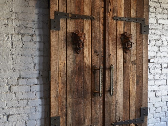 Photo of old doors made of wood and iron hanging on brick wall.