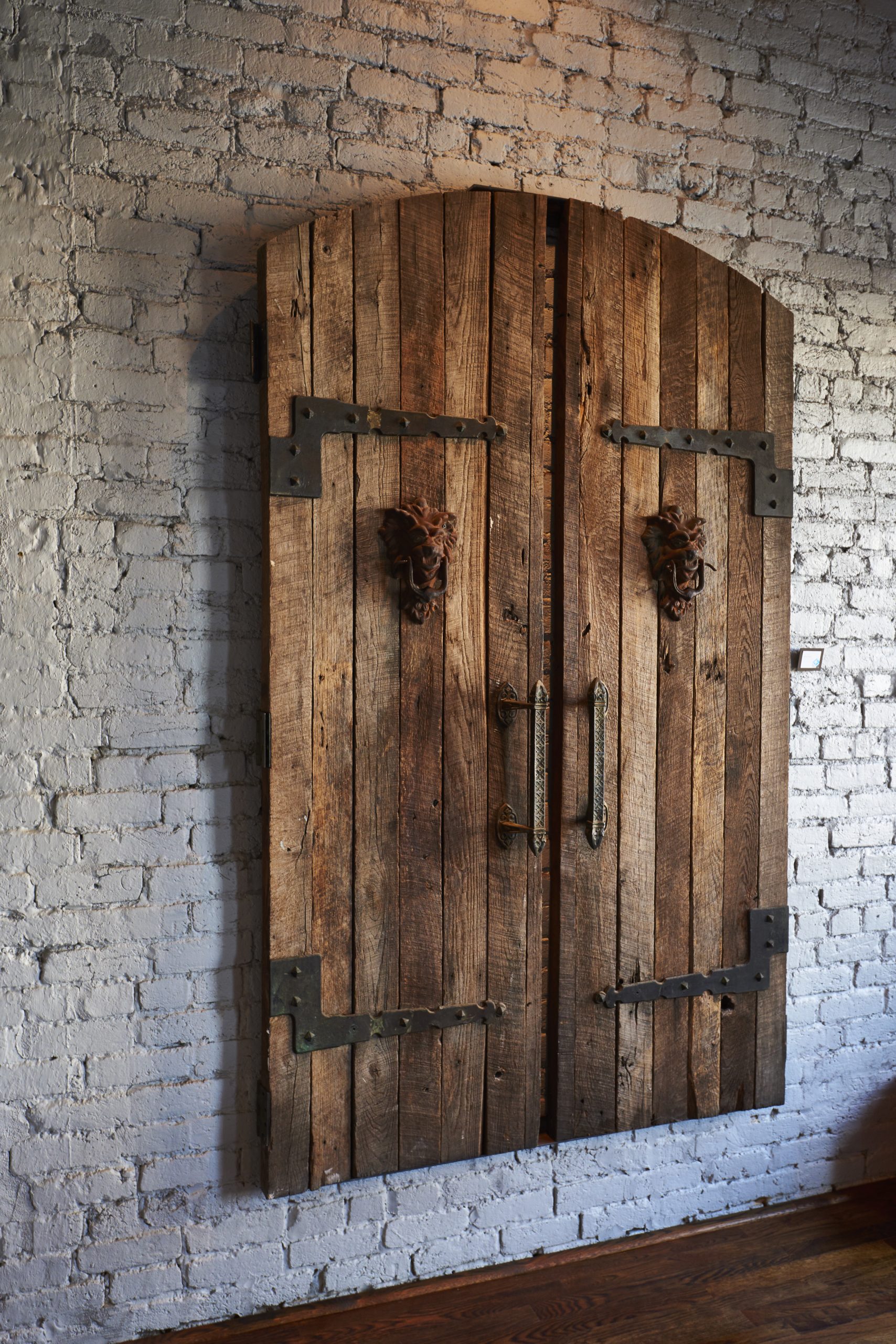 Photo of old doors made of wood and iron hanging on brick wall.
