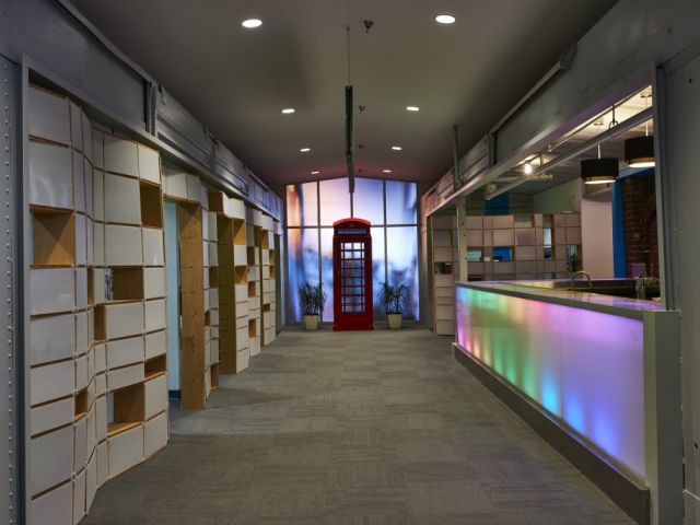 Photo of the area between the two box-cars inside Kinetic. Offices are on the right whereas a LED bar is on the left. An old red phone booth sits at the end.