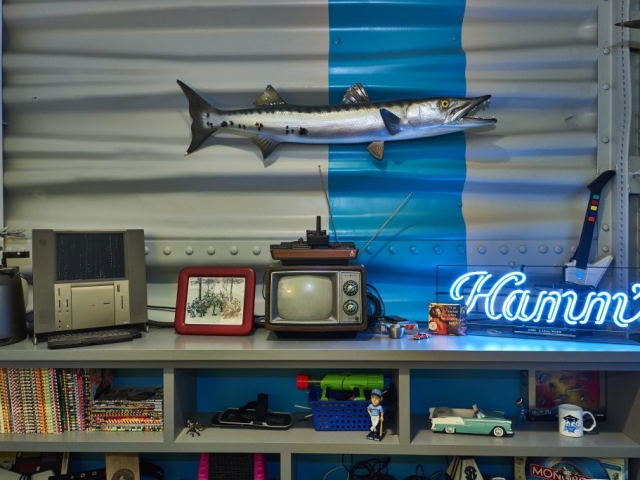 Photo of a collection of various memorabilia on a shelf with a fish on the wall above.